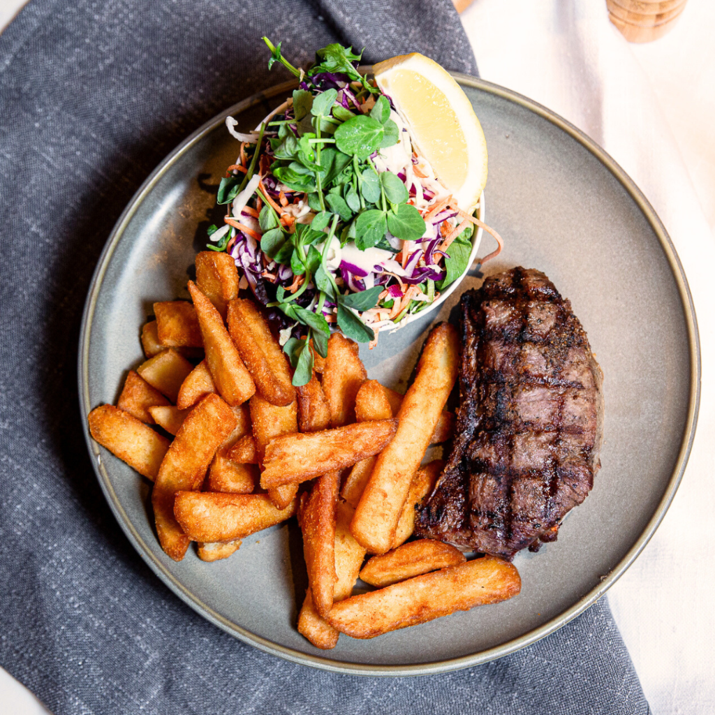 A plate with grilled steak, thick-cut fries, and a fresh salad topped with greens and a lemon wedge.