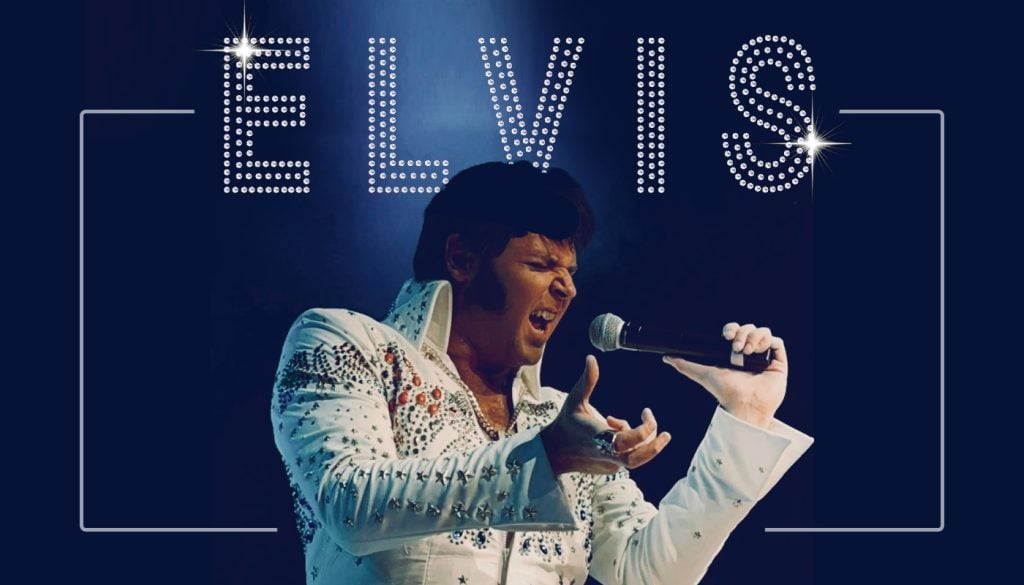 A man in an embellished white jumpsuit sings passionately into a microphone, with the word "ELVIS" in large, dotted lights above him on a dark background.