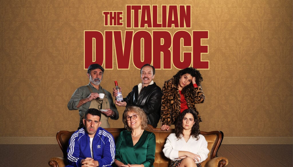 Six people pose on and behind a brown couch in front of a wall with large text reading "The Italian Divorce." The group displays varied expressions and outfits.