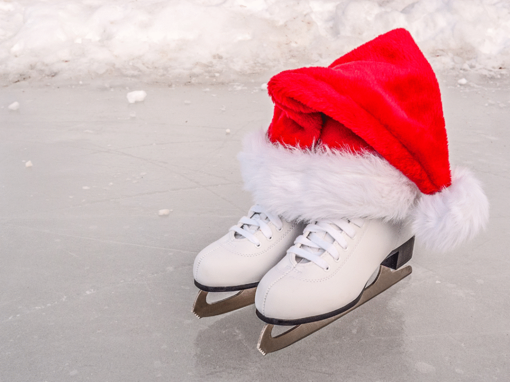 A pair of white ice skates on an ice rink, with a red and white Santa hat draped over them. Snow is visible in the background.