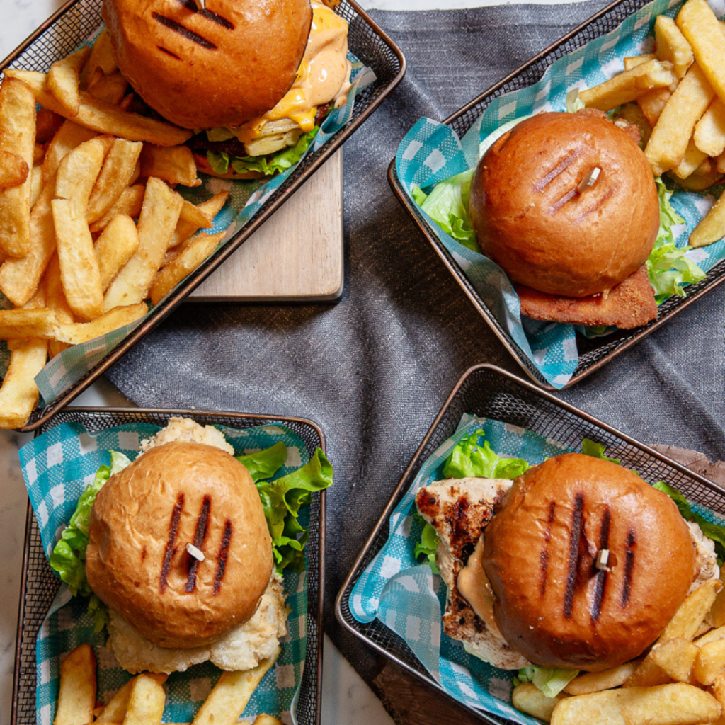 Four serving baskets with burgers and thick-cut fries, arranged on a table with green-checkered paper liners.