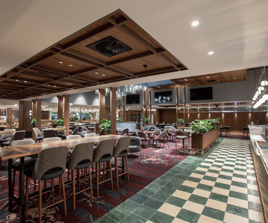 A modern restaurant interior with wooden ceiling, patterned carpet, green and white checkered floor, tables, chairs, and plants.