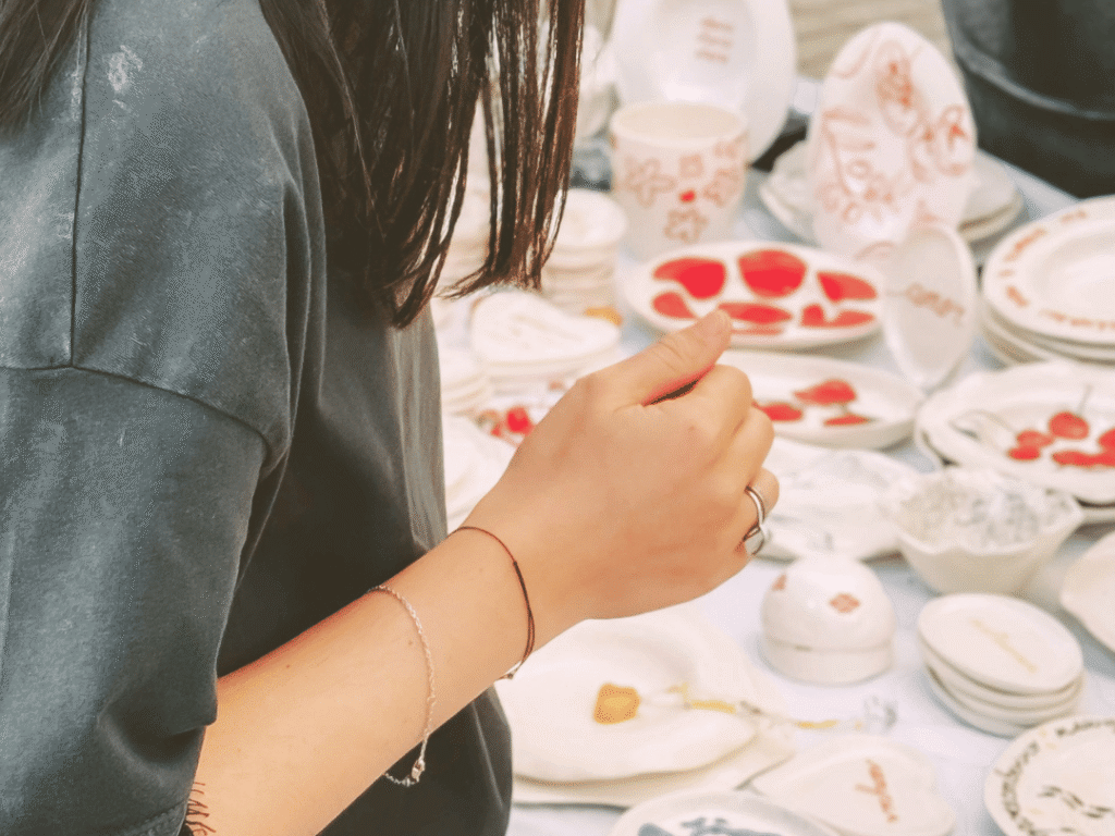 Person in a dark shirt stands near a table displaying various ceramic dishes and plates with colorful designs.
